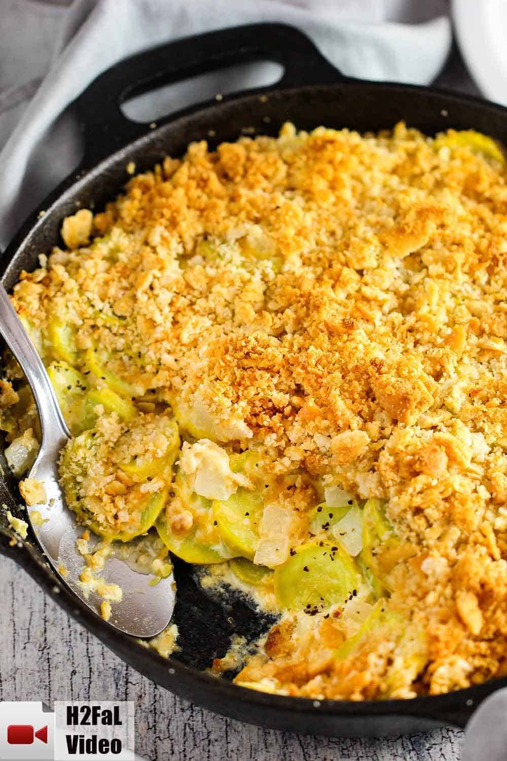 A large black cast iron skillet of yellow squash casserole with a serving spoon inserted in the dish. 