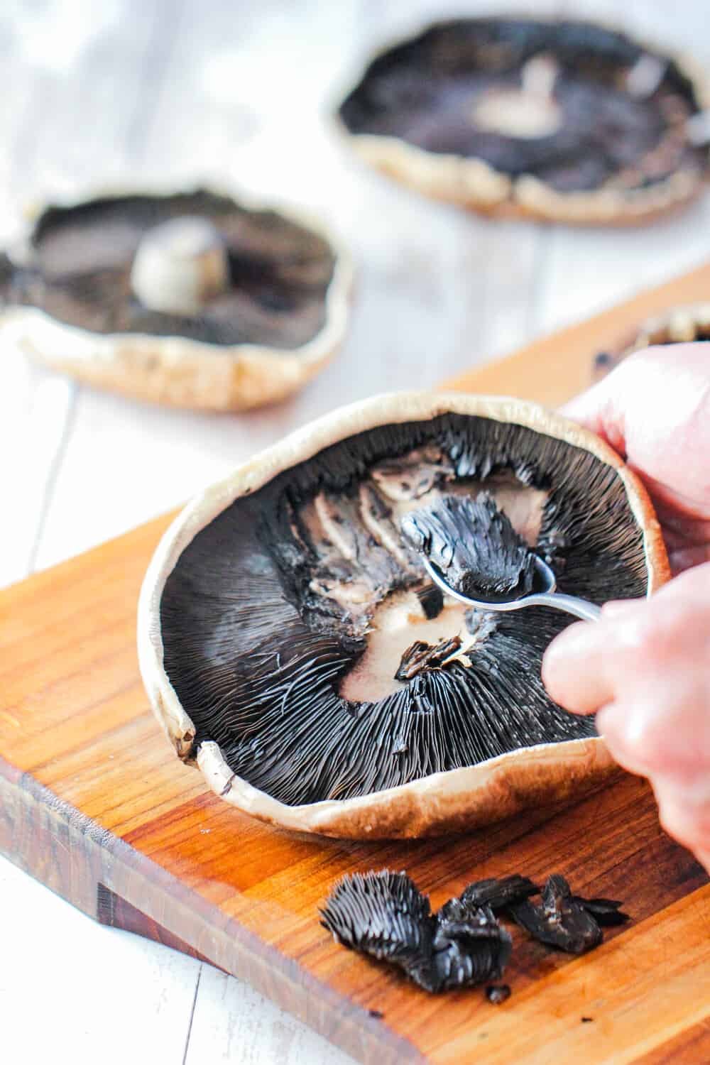 A hand using a spoon to scrape out the gills of a portobello mushroom cap.