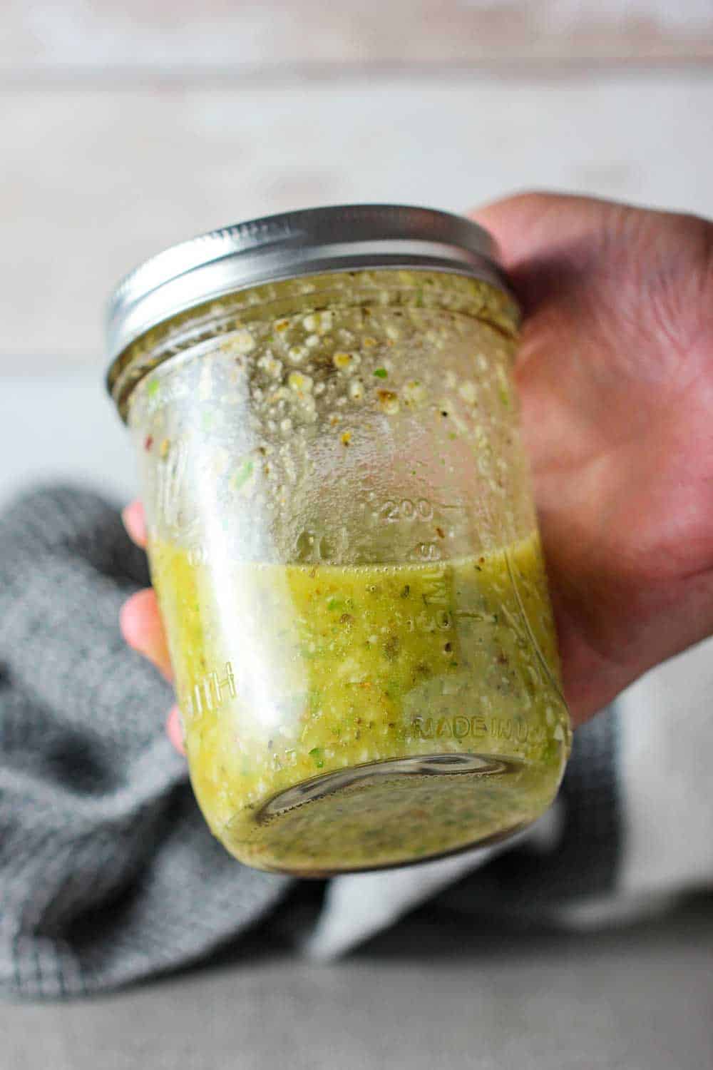 A hand holding a jar of Italian dressing that has been emulsified. 