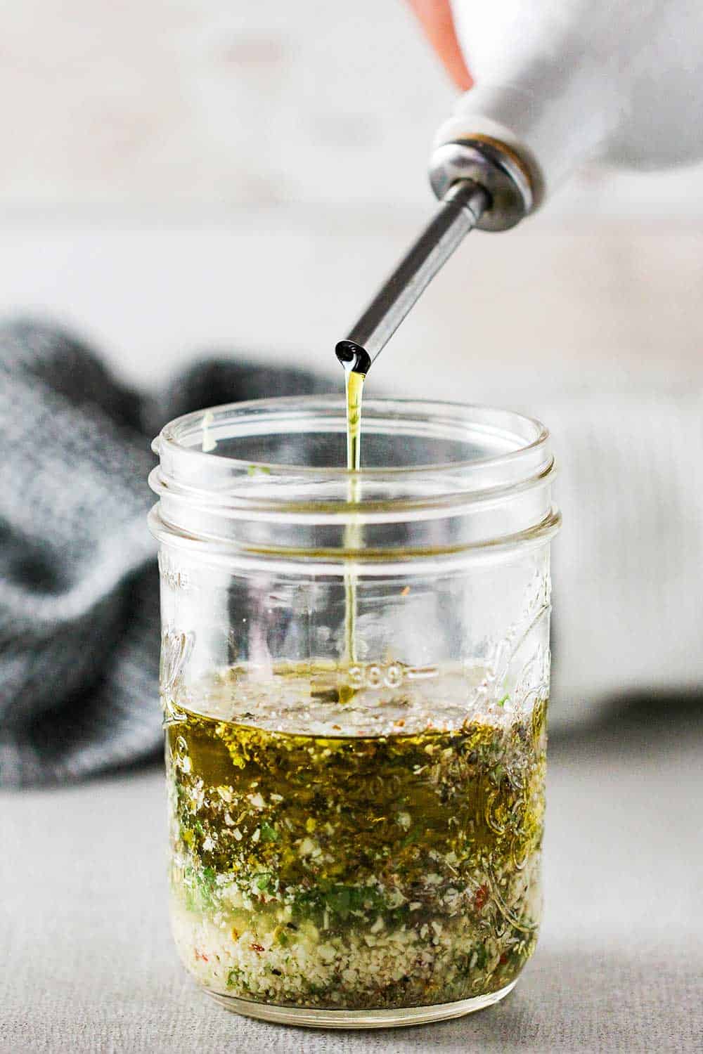 Extra-virgin olive oil being poured into a jar with Italian dressing ingredients. 