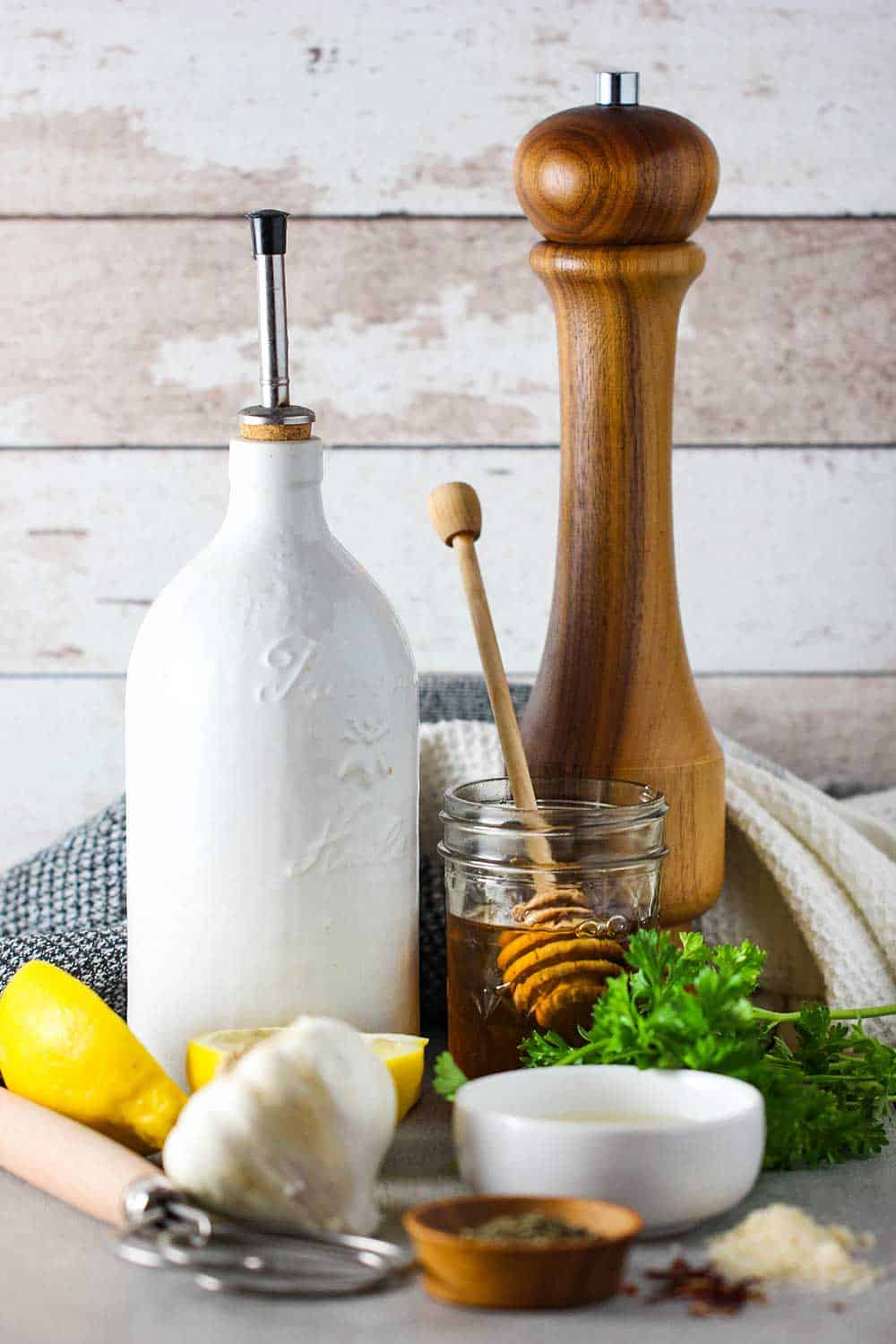 Extra virgin olive oil, a pepper grinder, lemon, honey, parsley and garlic on a white table. 