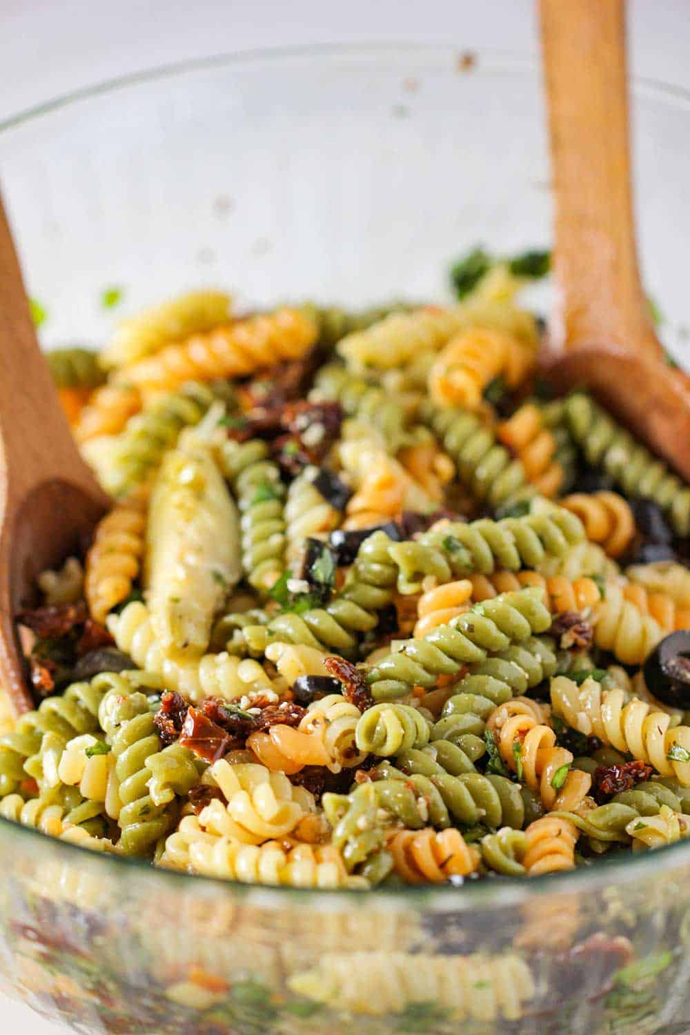 Classic Pasta Salad in a glass bowl with wooden spoons in it. 