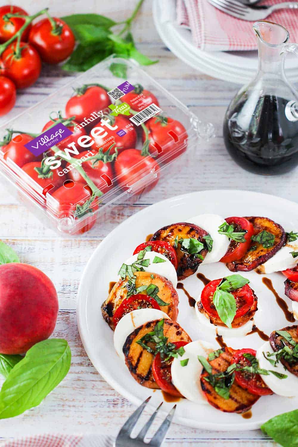 Caprese salad with grilled peaches on a white plate next to a package of campari tomatoes.