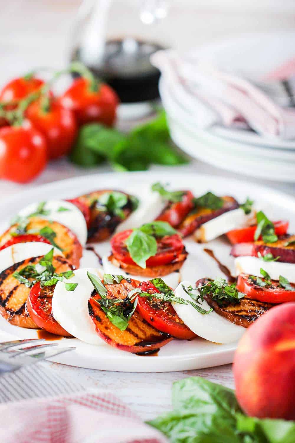 Caprese salad with grilled peaches on a white circular dish. 