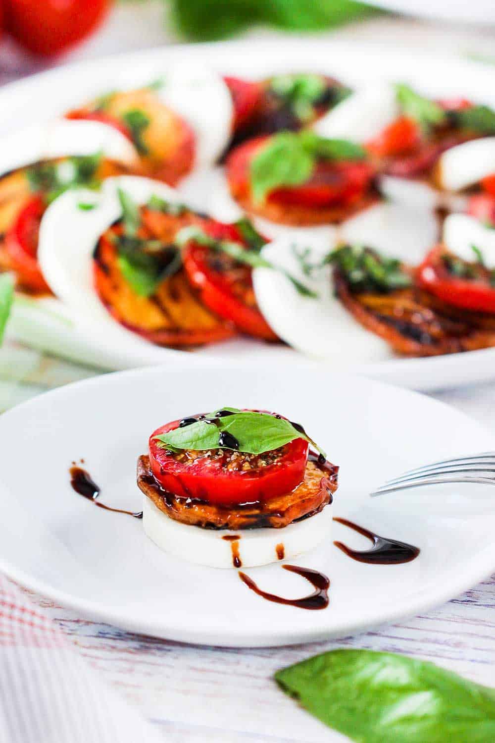 A single serving of caprese salad with grilled peaches on a white cocktail plate. 