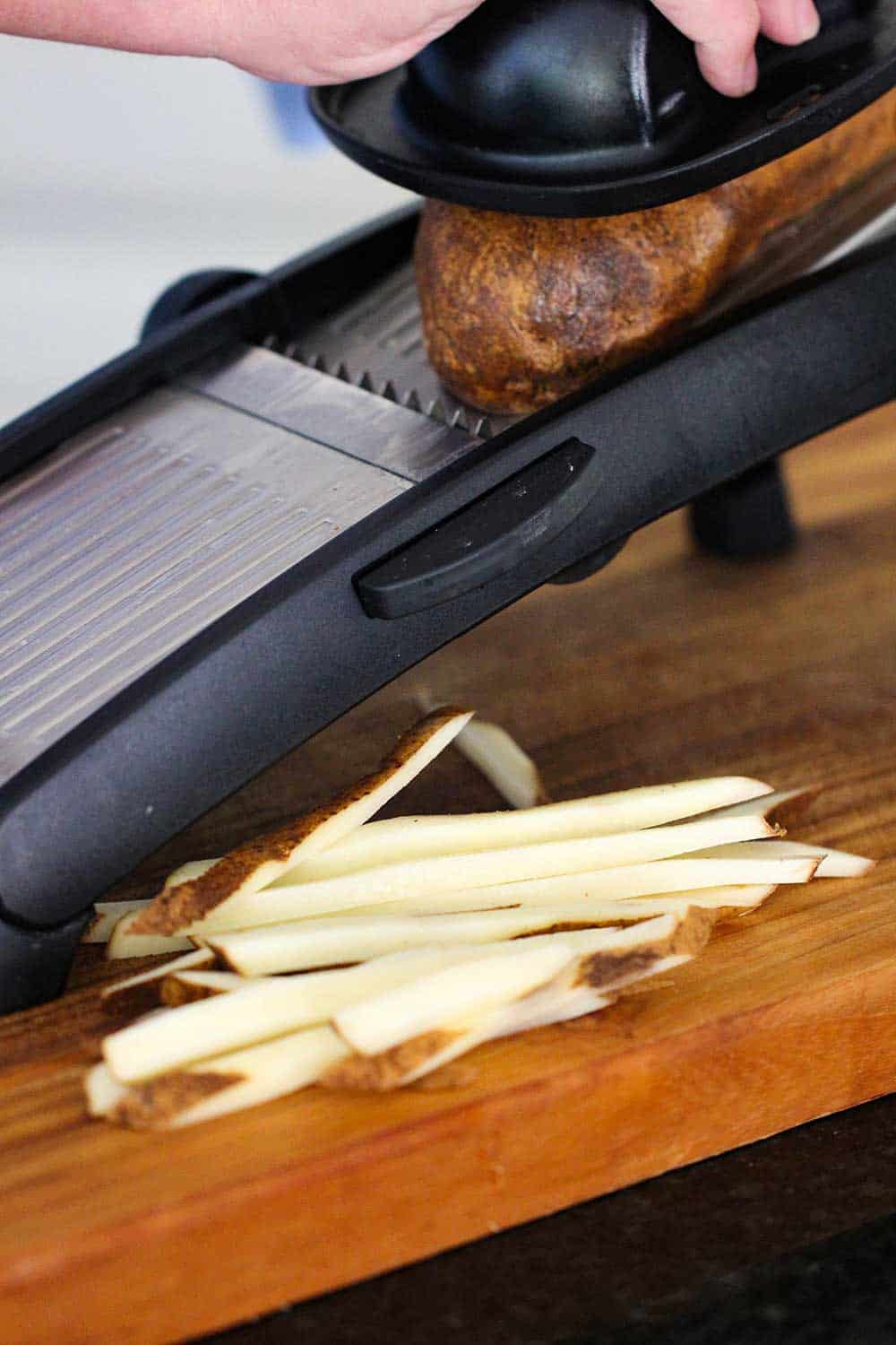 A large russet potato being cut on a mandolin for homemade French fries. 