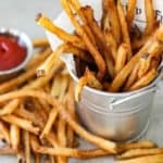 A small silver pale holding homemade French fries with a small bowl of ketchup nearby.