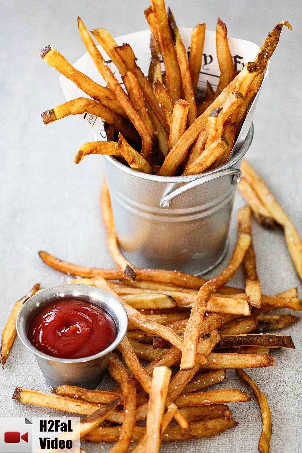 A silver pan holding homemade French fries next to a small container of ketchup. 