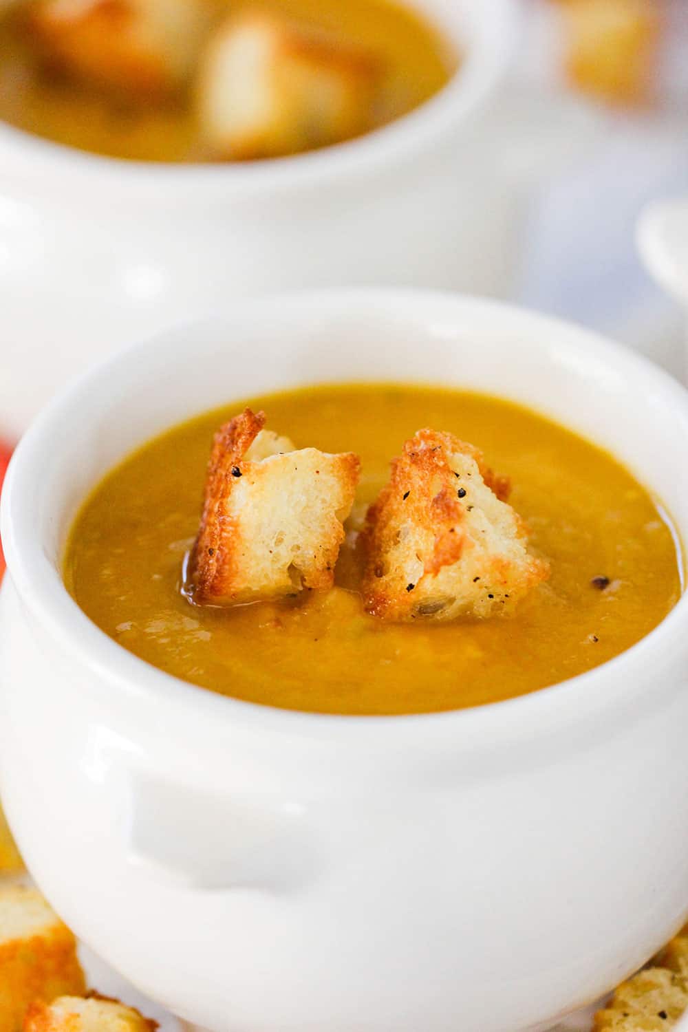 A white crock holding a bowl of butternut squash soup with two croutons on top. 