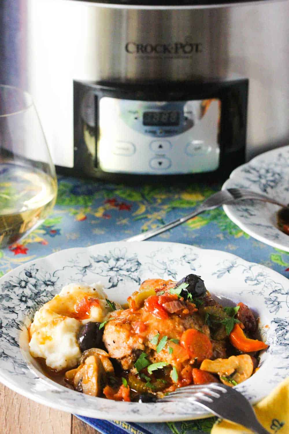 A small bowl of Provençal Chicken Stew in front of a stainless steel Crock-Pot. 