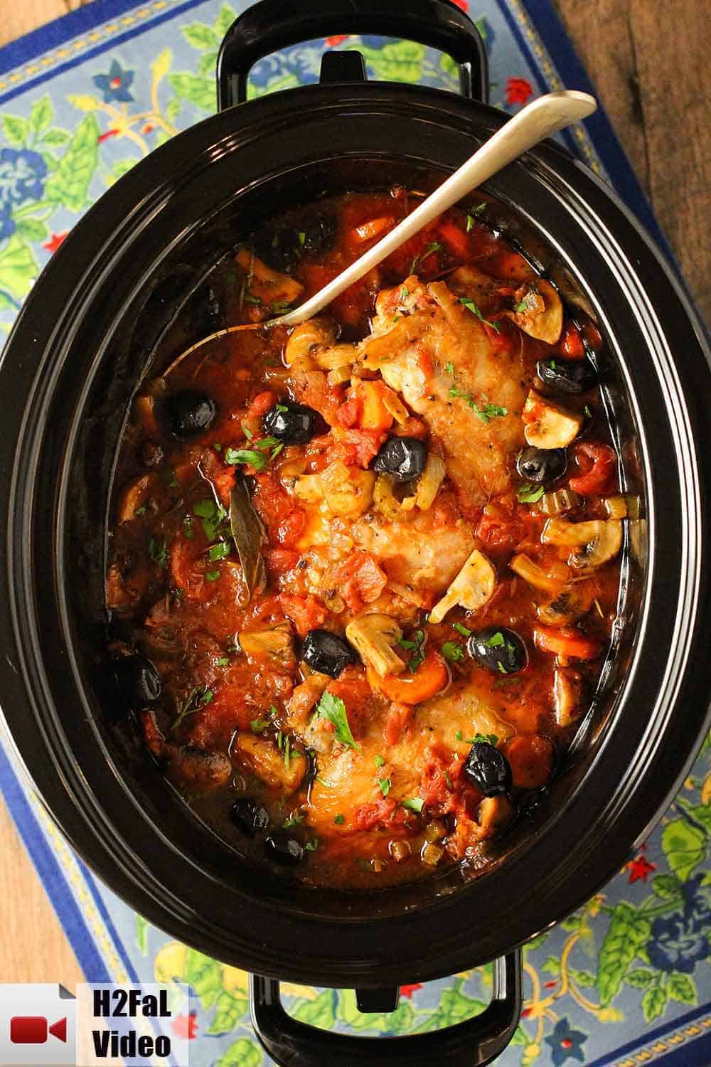 A large black slow-cooker filled with Provençal chicken stew on a floral place mat. 