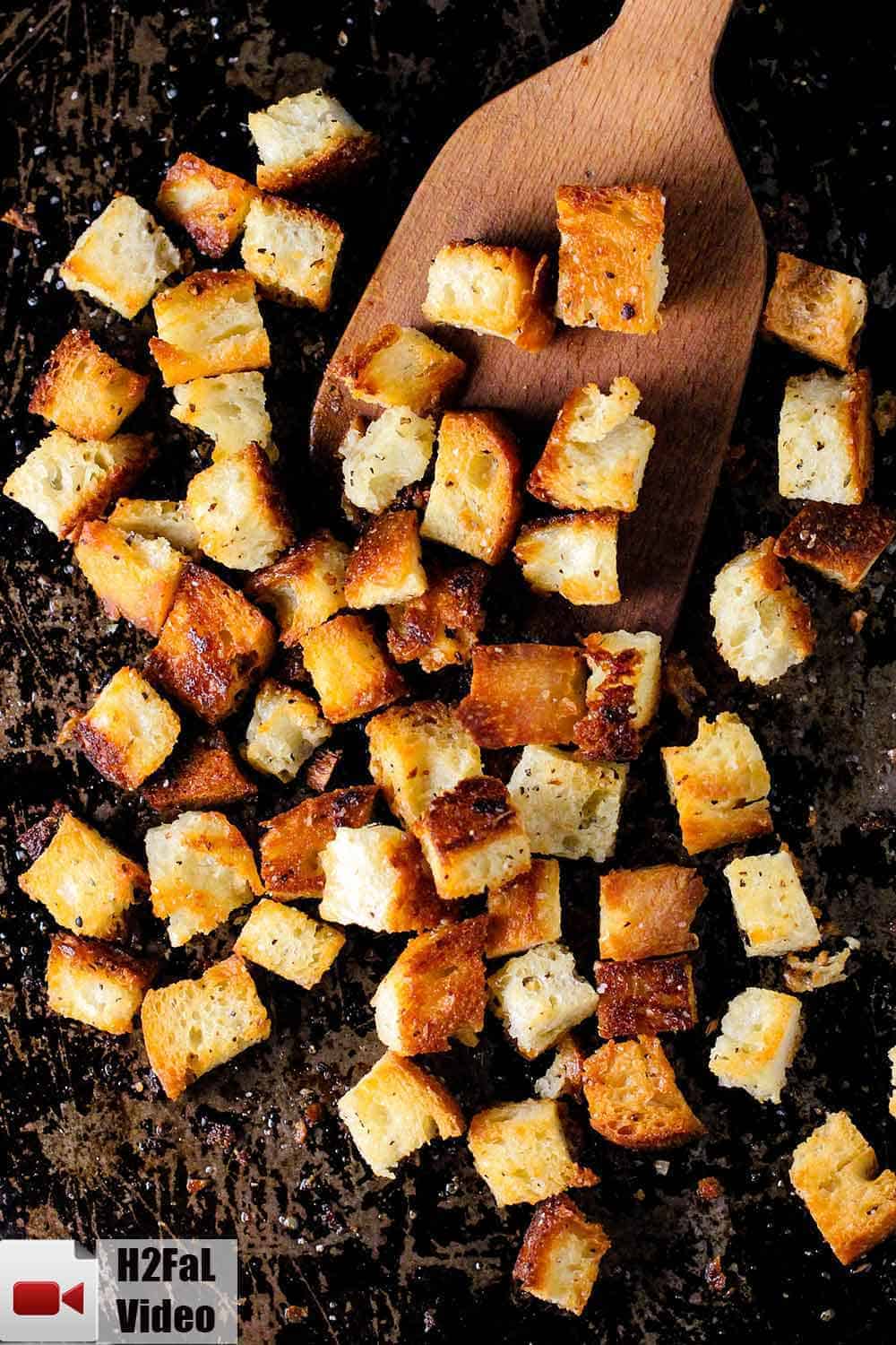A scraped baking sheet with homemade croutons on it and a wooden spoon. 