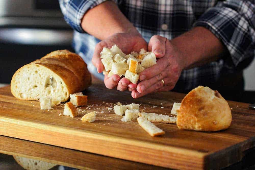 Two hands holding cubes of bread for homemade croutons. 