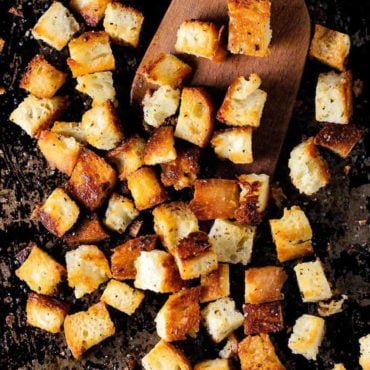 homemade croutons on a scraped black baking sheet with a wooden spoon.