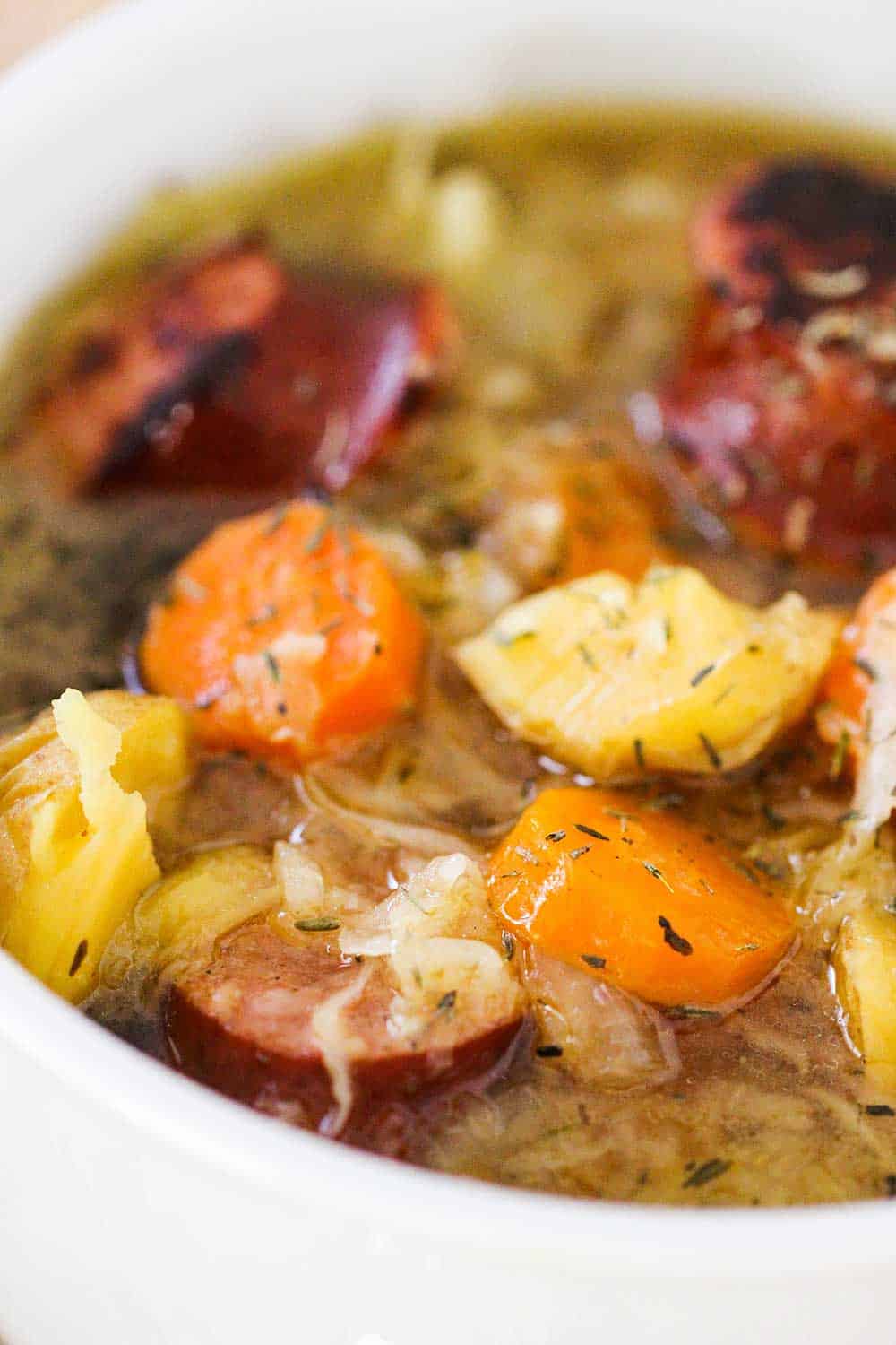 A close up view of a bowl full of stew with sausage, potatoes and carrots. 