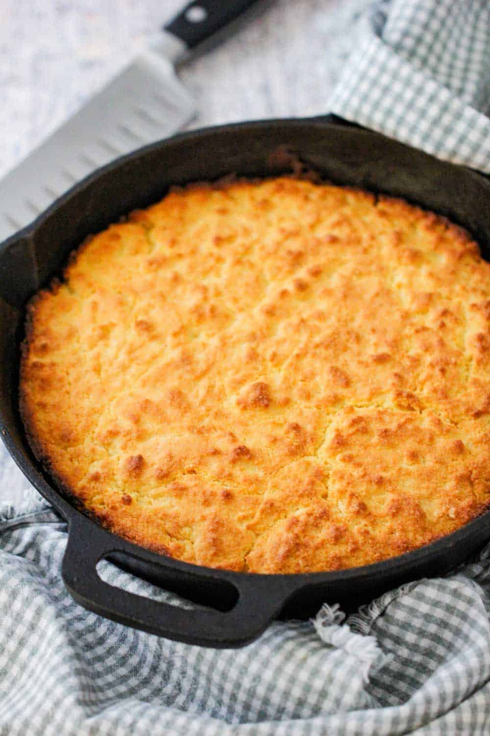 Homemade cornbread in a cast iron skillet with two patterned napkins nearby. 