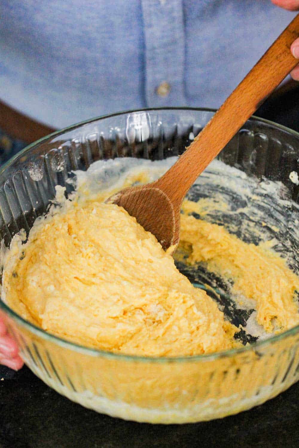 A hand using a wooden spoon to mix together batter for homemade cornbread. 