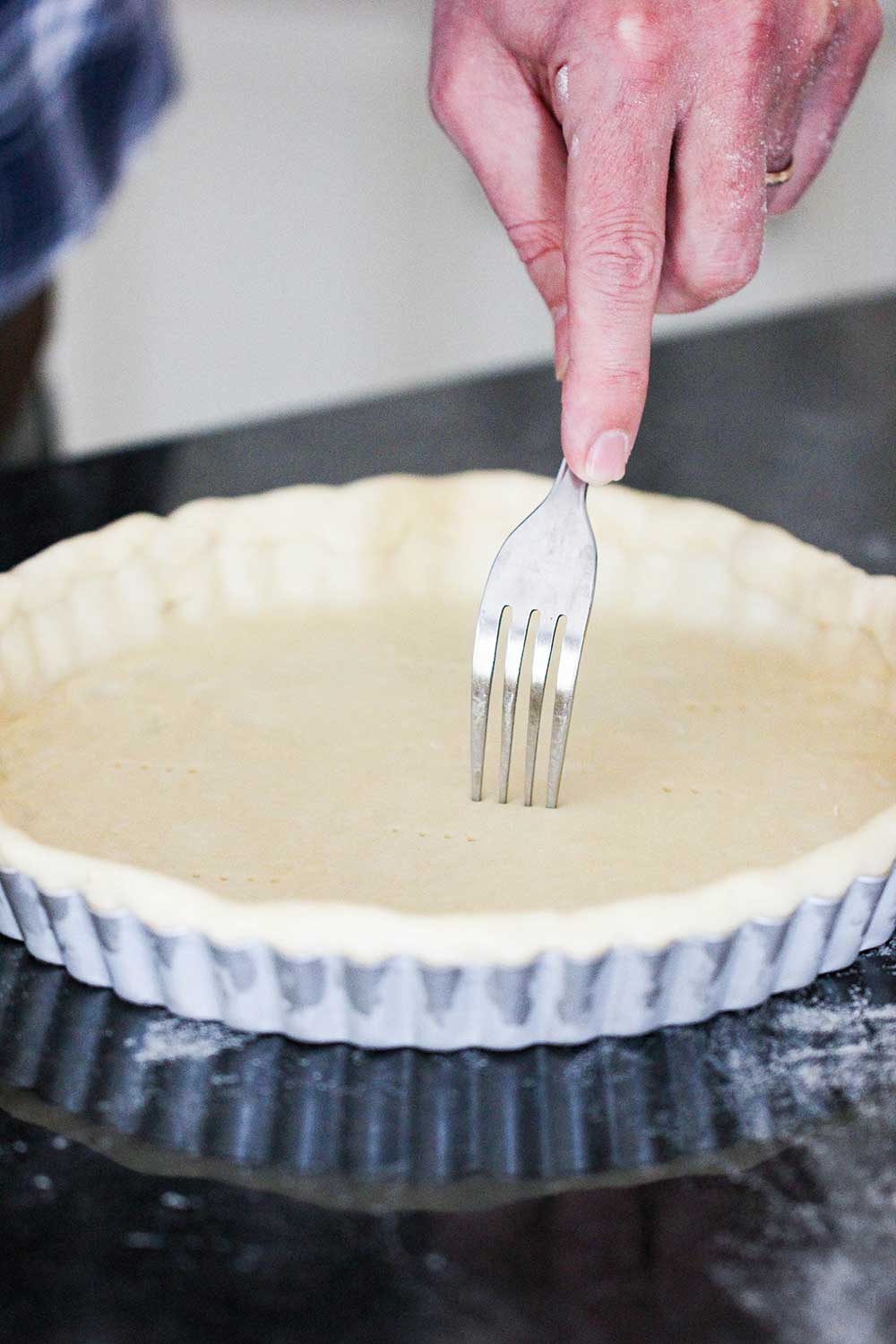 A hand using a fork to poke holes into pie dough that is in a tart pan. 