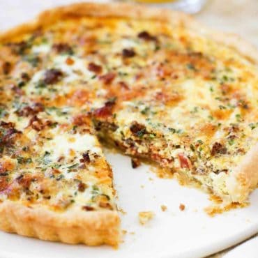 A breakfast quiche on a white serving platter with a slice removed.