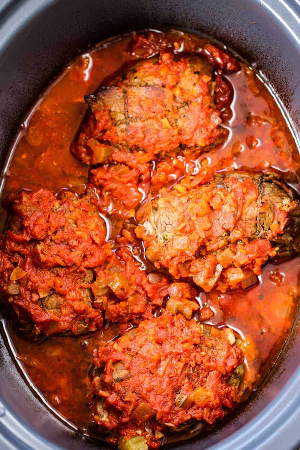 An overhead view of slow cooker beef braciole in a large Crock Pot. 