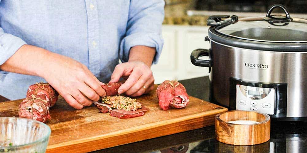 Two hands rolling up stuffed round steak on a large cutting board. 