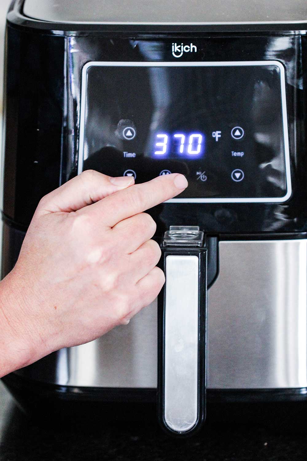 A finger pressing the temperature control on an air fryer. 