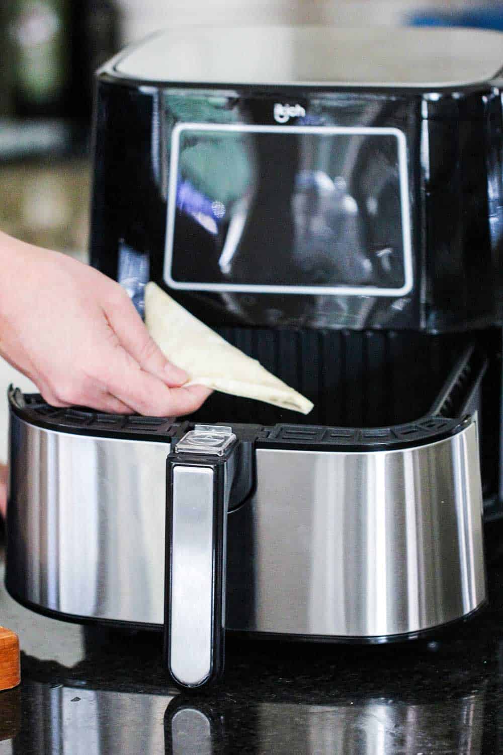 A hand lowering a phyllo triangle into an air fryer basket. 