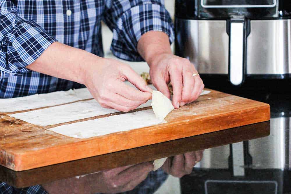 Two hands folding phyllo dough with a filling to form a triangle. 