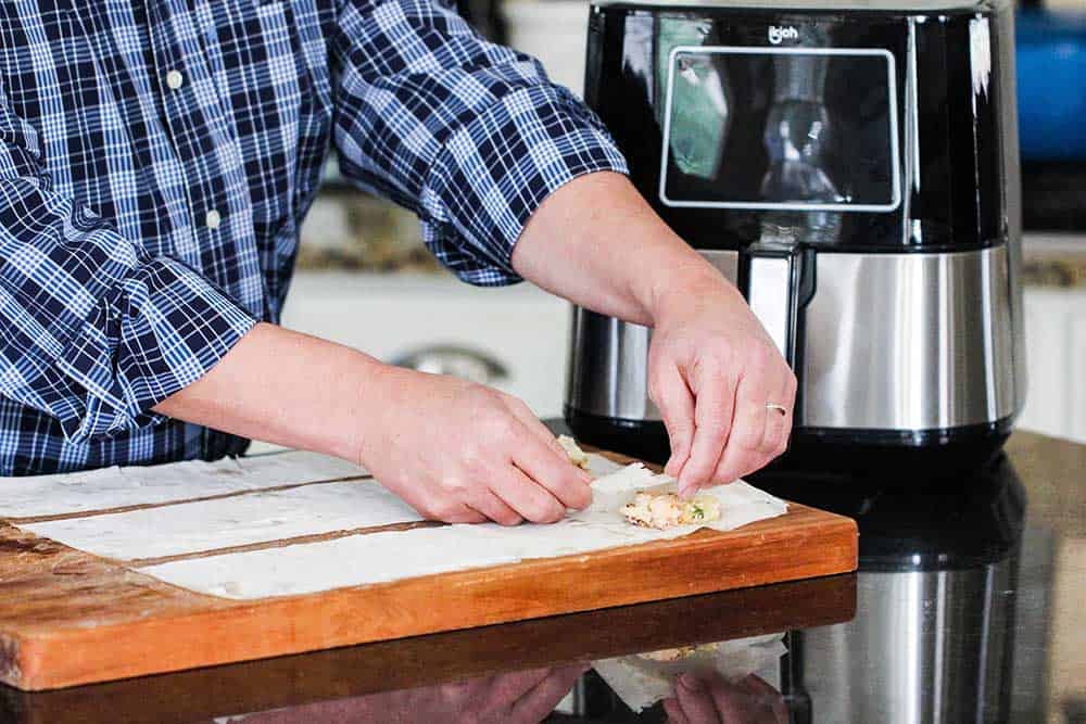 Two hands folding a strip of phyllo dough over a filling to start a triangle. 