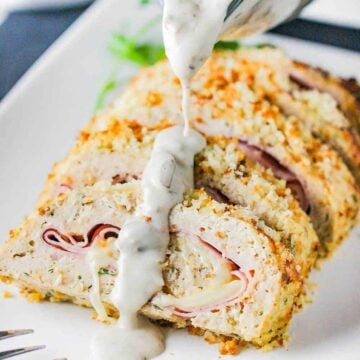 A white platter holding sliced cordon bleu meat loaf with a mushroom gravy drizzled over the top.