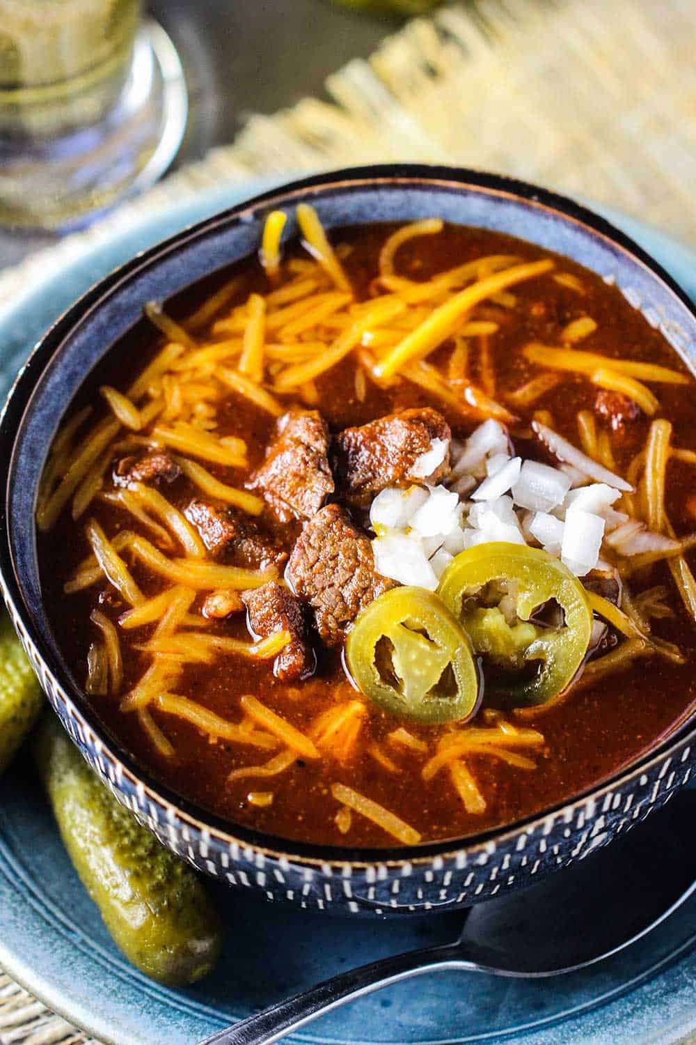 An overhead view of a large bowl of chili topped with shredded cheddar, onions, and jalapenos.