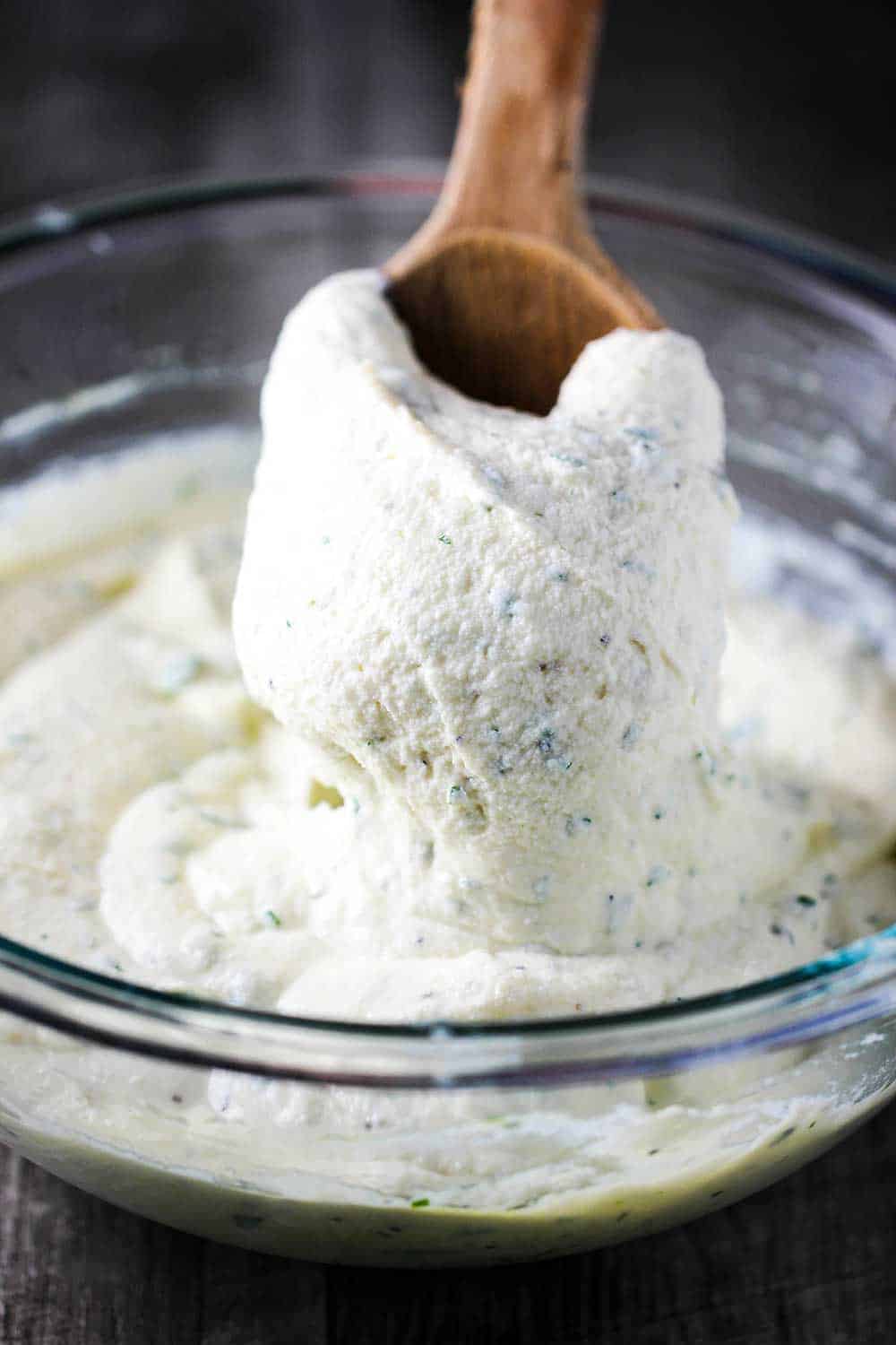 A large bowl of ricotta cheese with a wooden spoon lifting a heaping amount out of the bowl. 