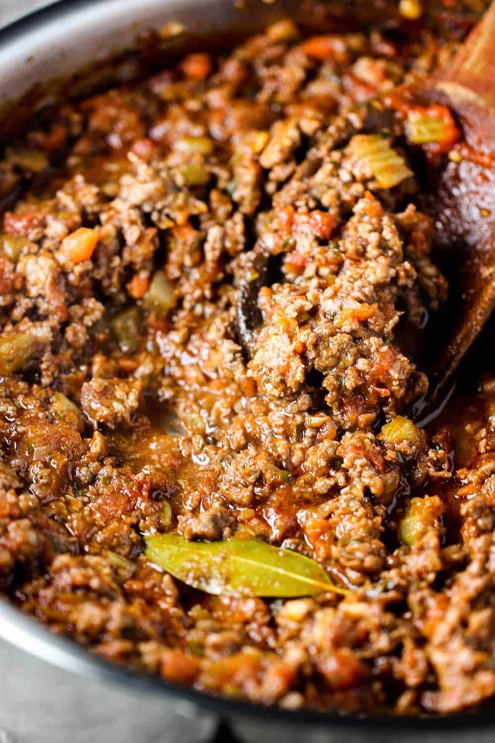 A large saucepan filled with meat sauce with a wooden spoon in it. 