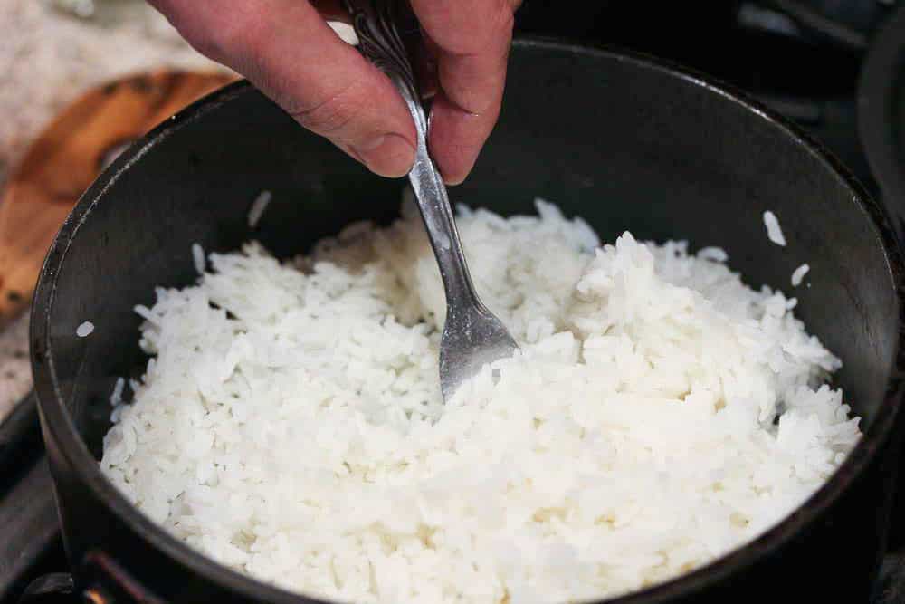 A hand fluffing perfect steamed rice in a pan to fluff the rice. 