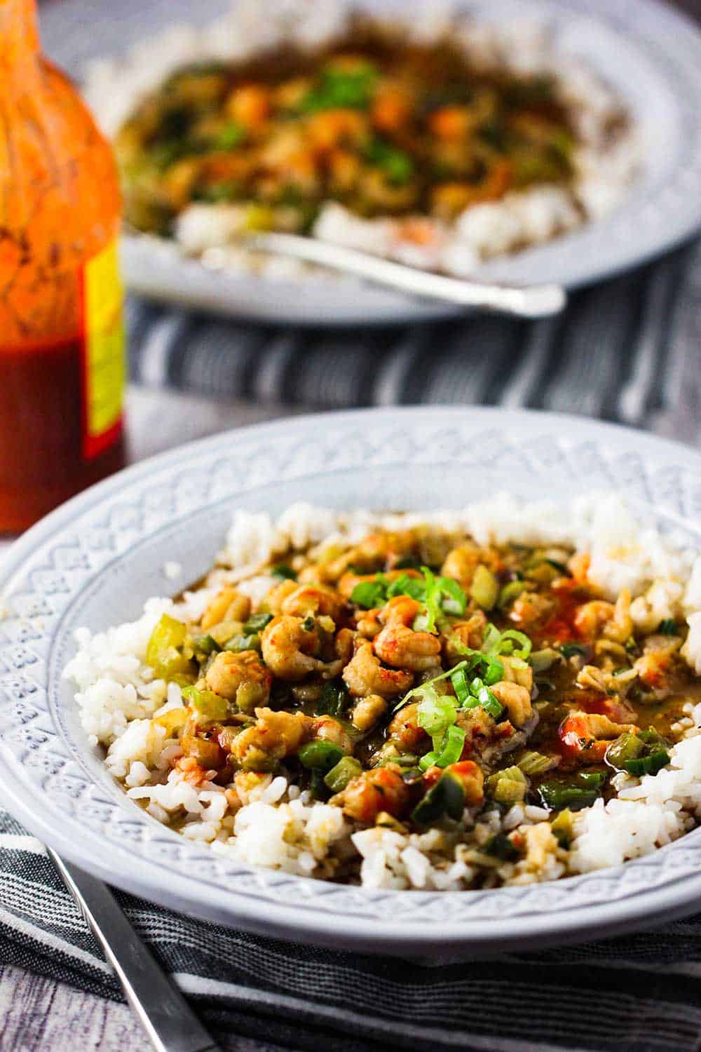 Two grey bowls filled with crawfish etouffee with a bottle of hot sauce nearby. 