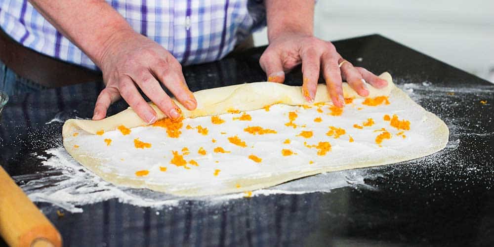Two hands rolling dough for homemade orange sweet rolls.