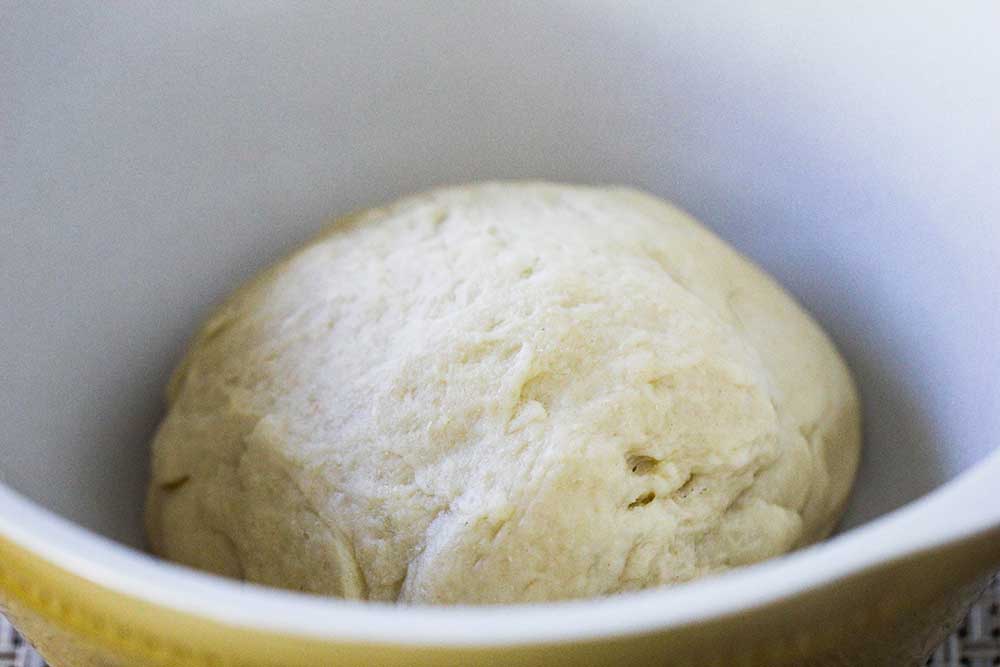 A ball of dough sitting a ceramic bowl.