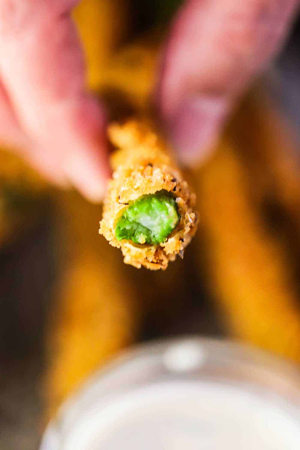 A hand holding a fried asparagus stalk that has been bitten in half. 