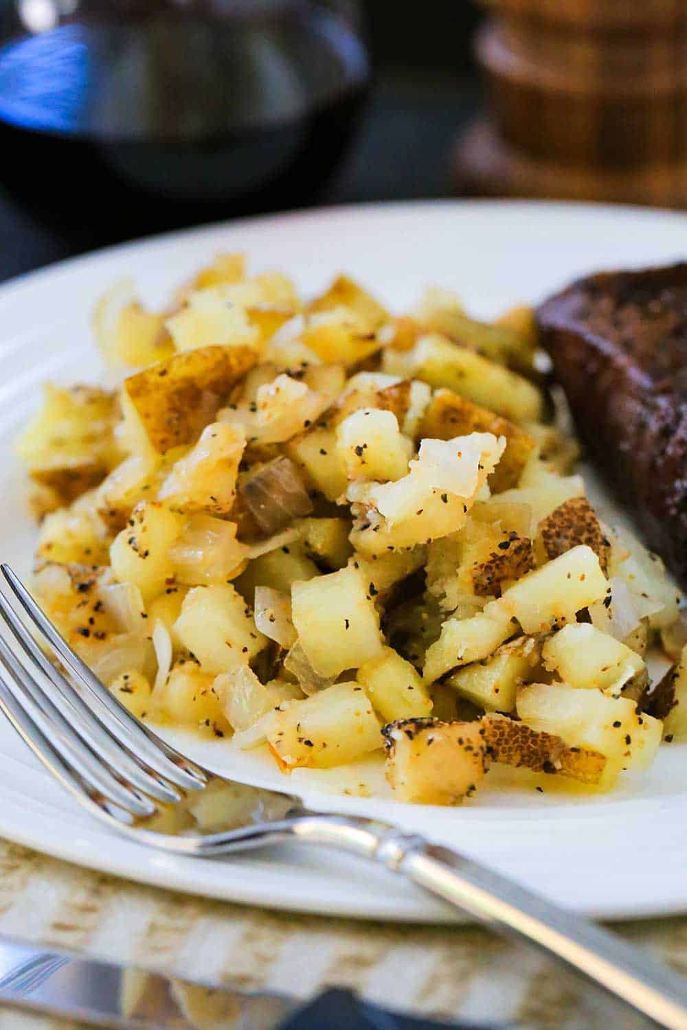 A close up view of a white dinner plate loaded with roasted potatoes in foil next to a grilled steak. 