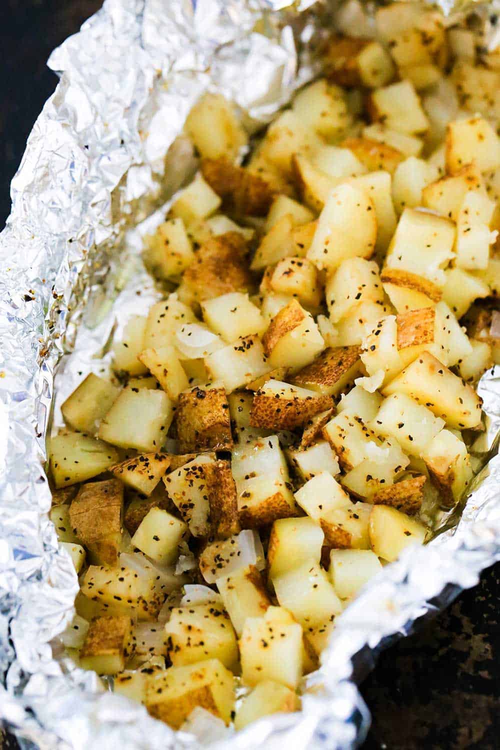 A foil packet filled with cubed roasted potatoes in foil on a baking pan. 