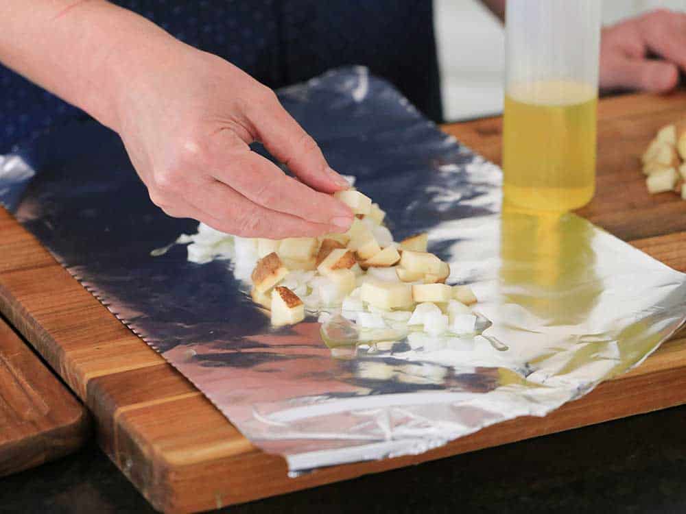 Two hands placing cubed potatoes on a piece of foil for oven-roasted potatoes in foil. 