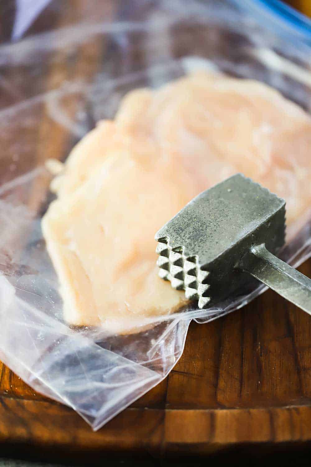 A mallet turned on its side on a chicken breast in plastic freezer baggie.