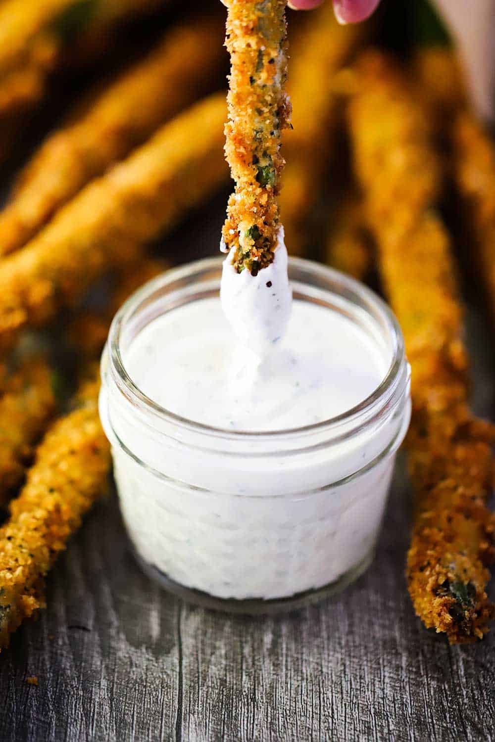 The tip of a fried asparagus being dipped into a small jar of homemade ranch dressing. 