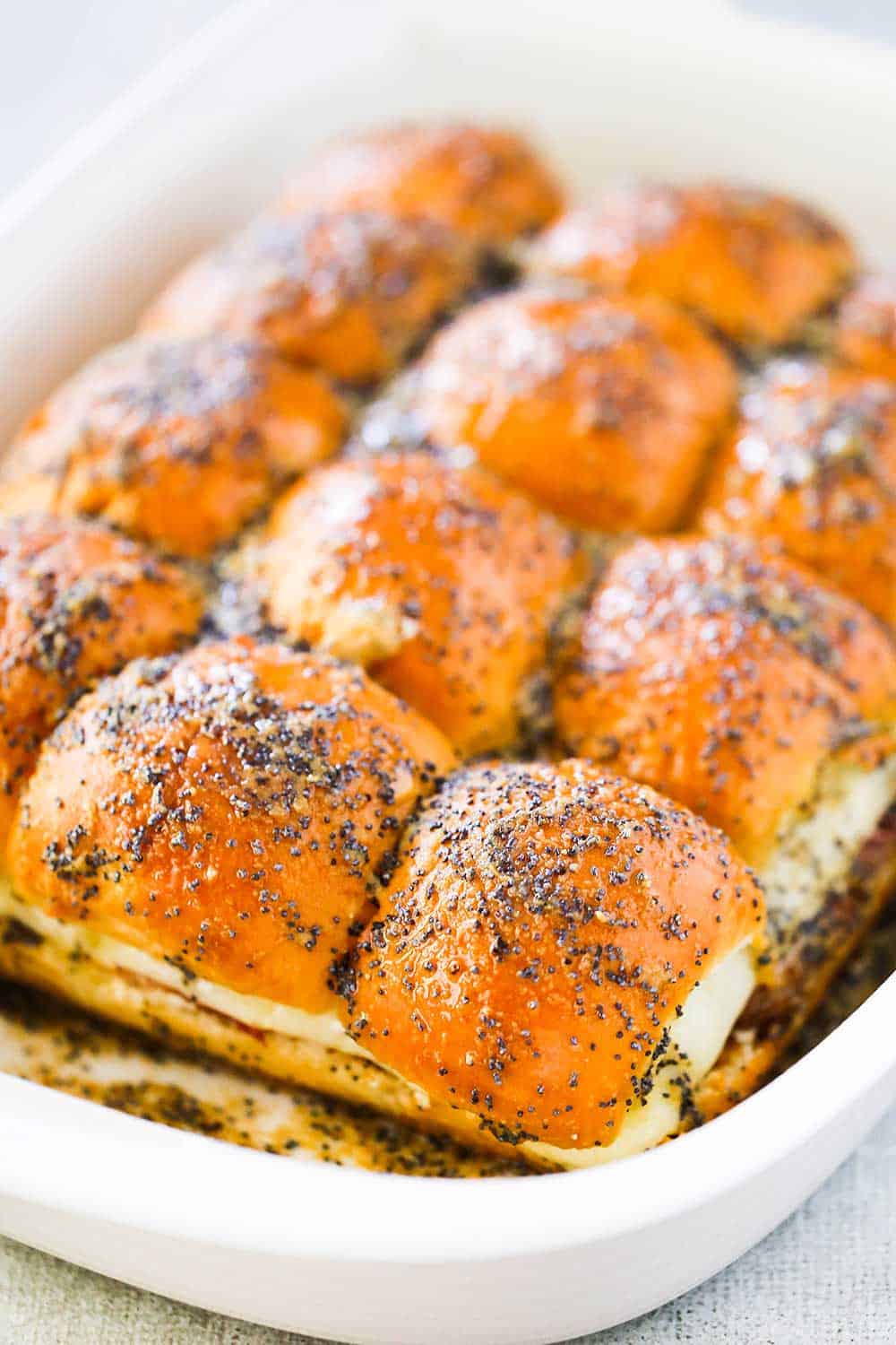 A white baking dish filled with baked ham and Swiss sliders. 