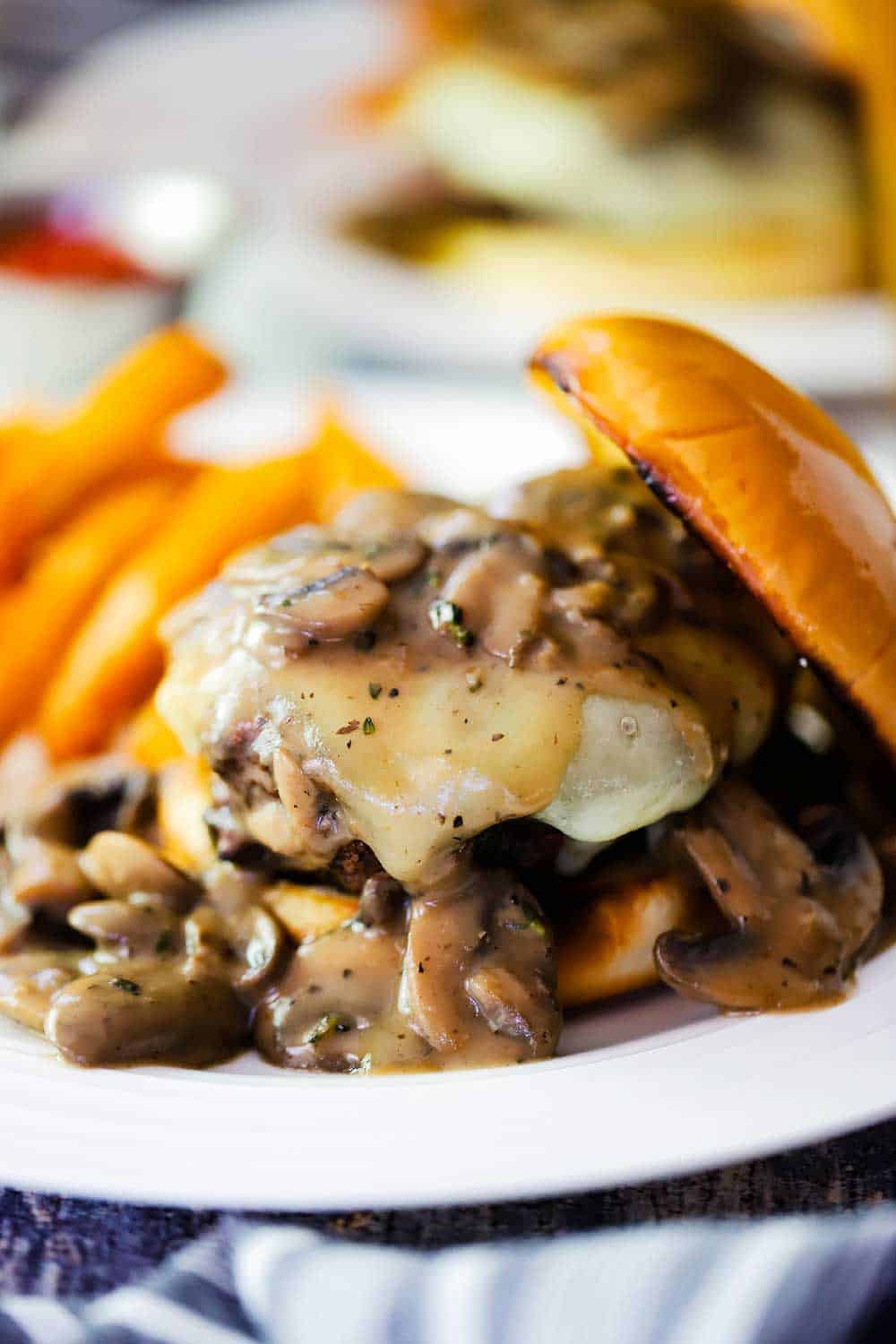 A close up view of a mushroom Swiss burger on a white plate with a pile of French fries next to it. 