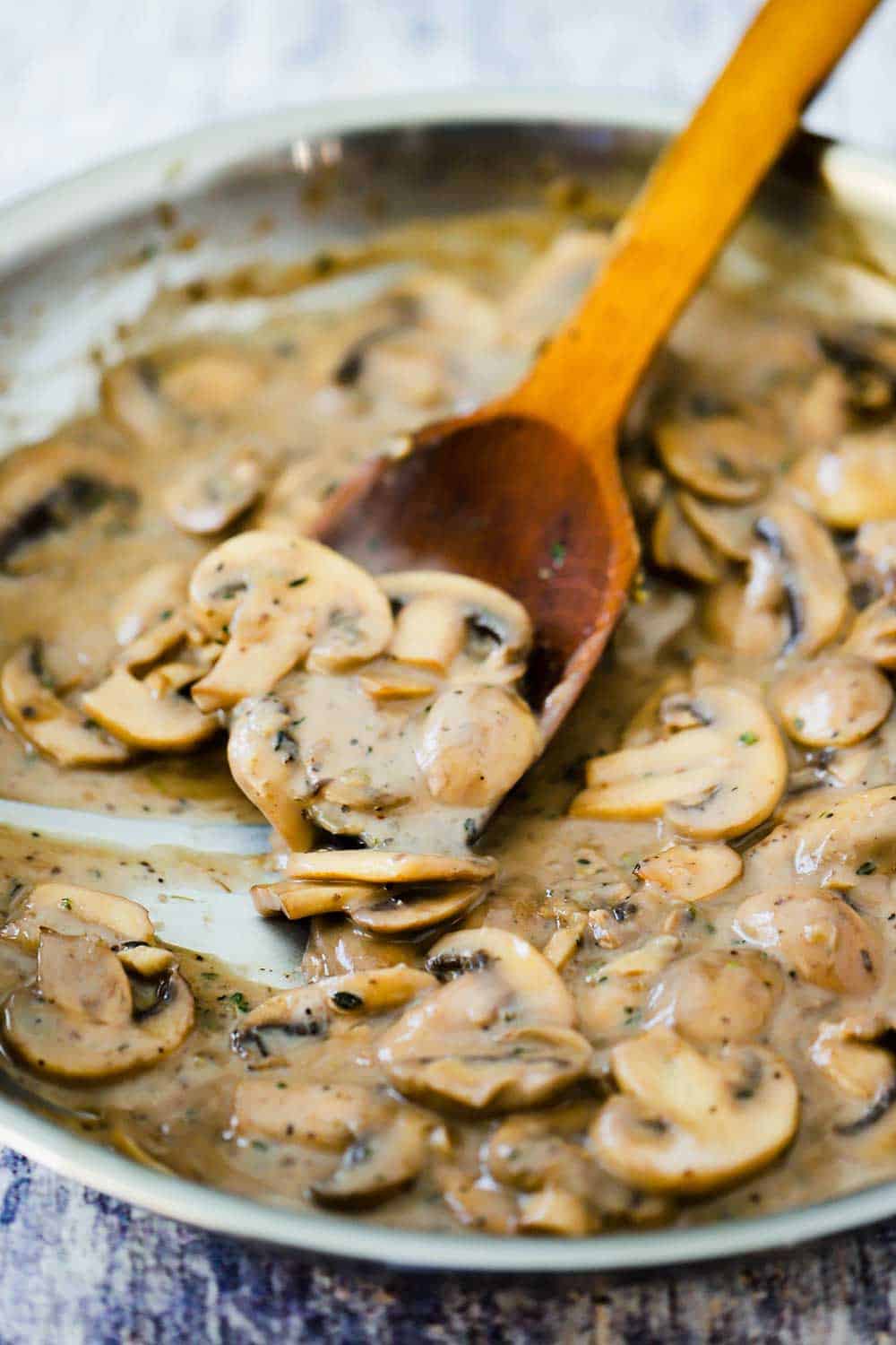 A large skillet filled with a mushroom sauce with a wooden spoon in it. 