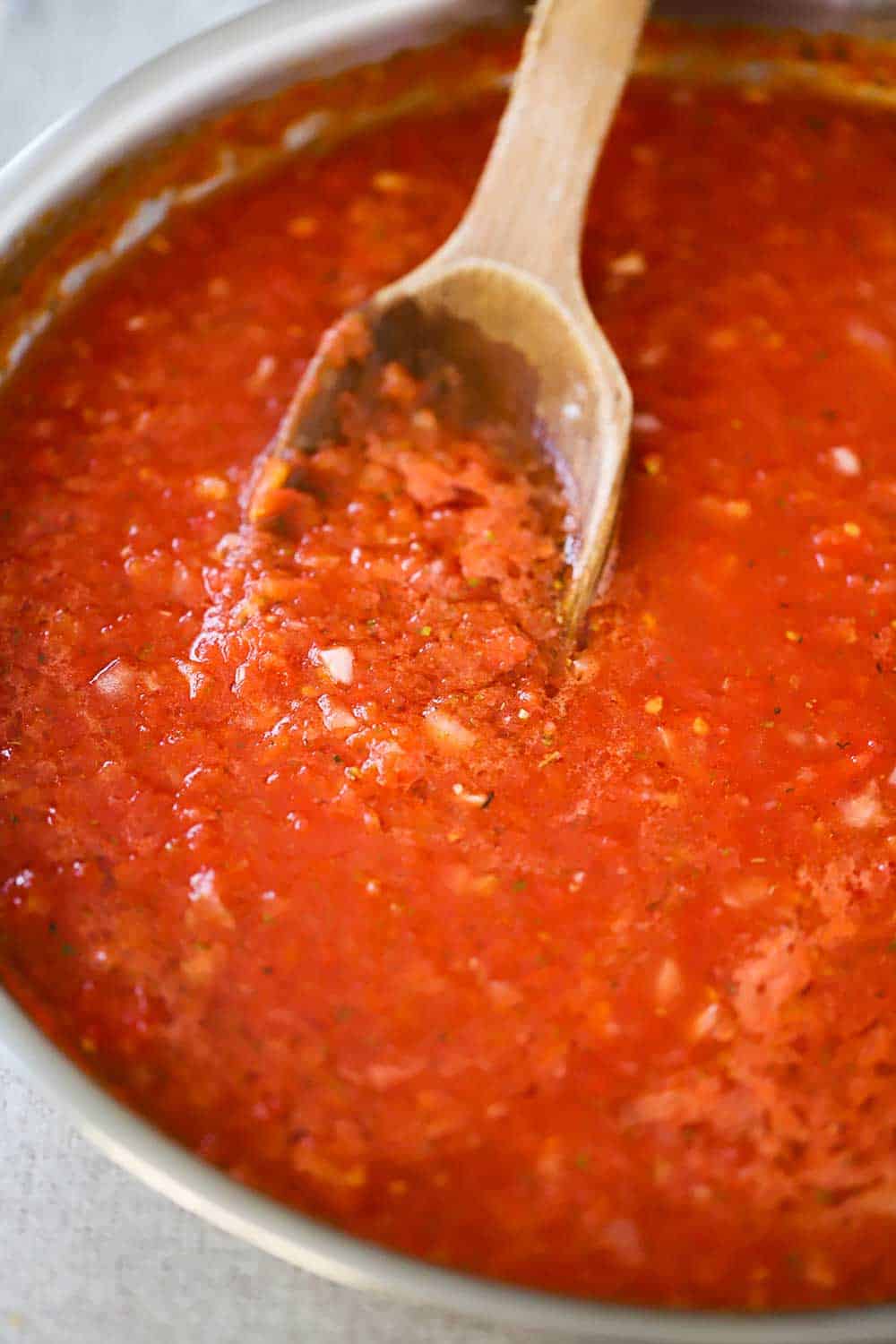 A large silver skillet filled with a red sauce with a wooden spoon in it. 