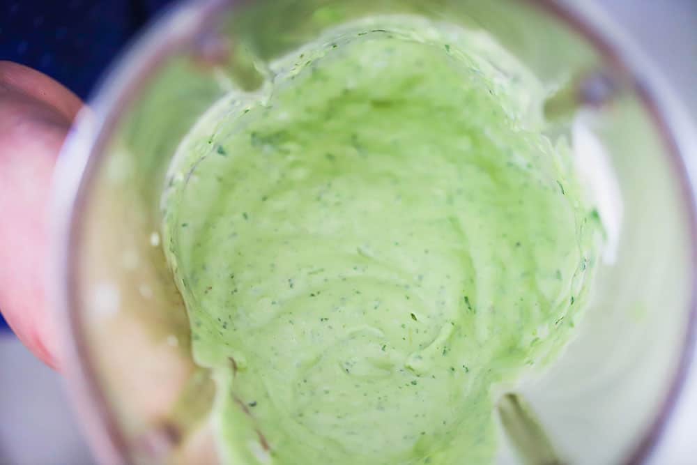 An overhead view looking into the bowl of a blender with an avocado dressing inside. 