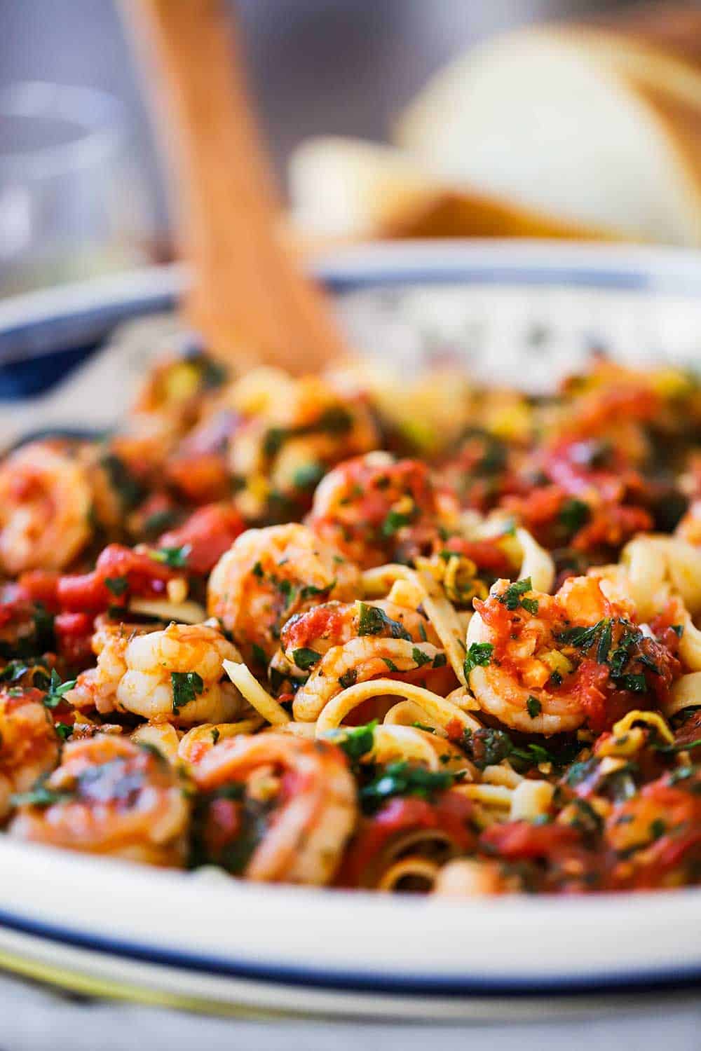 A close up view of a large pasta bowl filled with shrimp fra diavolo and a large wooden spoon inserted into it.