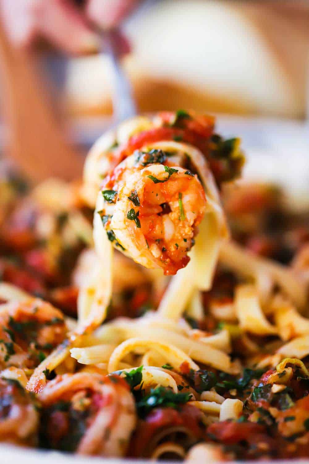 A hand lifting up a fork filled with shrimp fra diavalo from a bowl of the same.